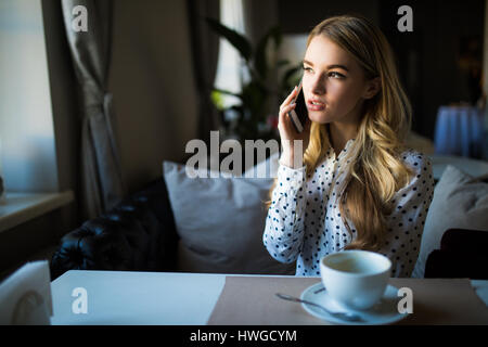 charmante Lady mit schönen Lächeln Gespräch am Mobiltelefon beim Sitzen im Café in der Mittagspause Stockfoto