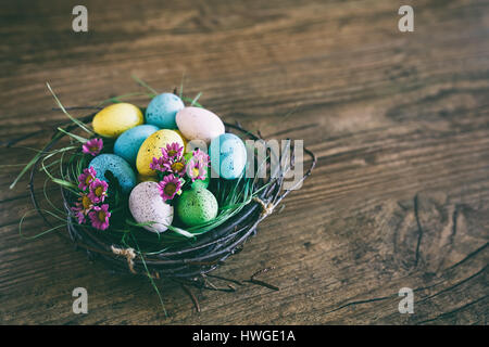Ostern-Hintergrund. Schönen bunten Eiern im Nest mit Frühlingsblumen über hölzerne dunklen Hintergrund Stockfoto
