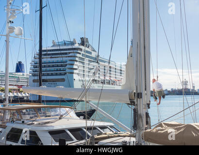 Seemann Klettern Mast Luxusyacht mit Kreuzfahrtschiff MSC Poesia im Hintergrund Stockfoto