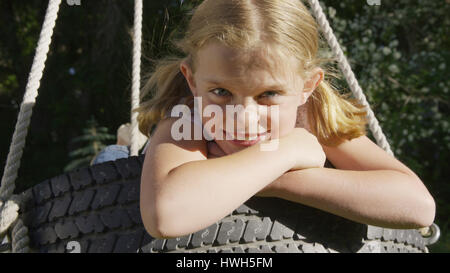 Porträt von lächelnden spielerische Mädchen sitzen auf Reifenschaukel hautnah Stockfoto