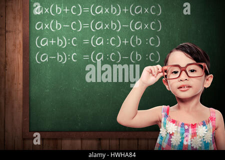 kleines Schulmädchen mit grünen Tafel mit mathematischen Formeln Stockfoto