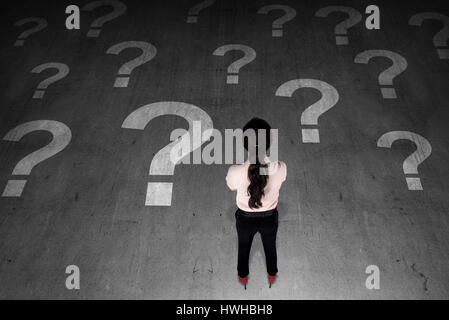 Asiatische Geschäftsfrau sucht Fragezeichen auf dem Boden. Sie denkt Stockfoto