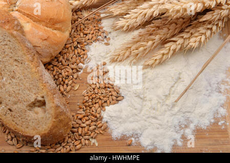 Körner, Ähren, Mehl, Brot und Bagel auf einem Holztisch. Konzept der Zubereitung von Essen aus Getreide, Rohstoff im fertigen Produkt. Rustikaler Hintergrund Stockfoto