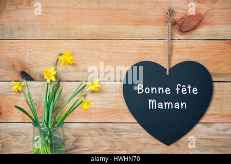 Bonne Fete Maman, Mütter Französisch, Tageskarte, Holzplanken mit Narzissen und einer Tafel in der Form eines Herzens Stockfoto
