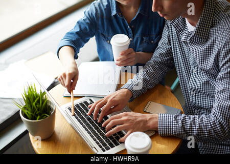 Nahaufnahme der beiden jungen Kollegen konzentrierte sich auf die Arbeit beim Sitzen an runden Holztisch und köstlichen Kaffee aus Pappbechern trinken Stockfoto