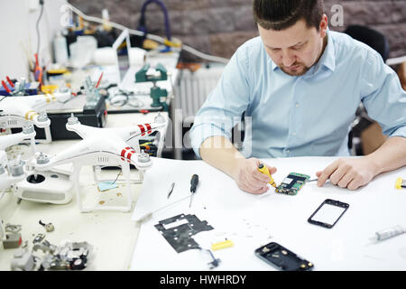 Hohen Winkel Schuss des modernen Menschen mobile Gerät auf Tisch mit verschiedenen disassemblierten Elektronik, Teile und Drohnen in modernen Werkstatt zu reparieren Stockfoto