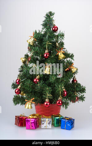 Ein faux Mini Weihnachtsbaum verziert mit Ornamenten und Glocken mit Geschenken unter in glänzendes Geschenkpapier. Stockfoto