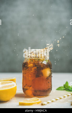 Im Sommer kalten Eistee mit frischer Bergamotte und Minze im Glas mit Spritzern, graue Betonwand im Hintergrund, Textfreiraum. Essen in Bewegung-Konzept Stockfoto