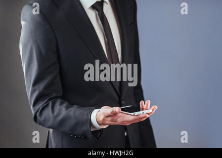 Geschäftsmann mit einem Handy in der Hand. Ein Student in einem Anzug auf einem dunklen Hintergrund Stockfoto