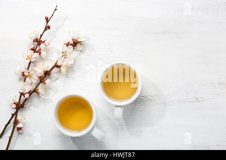 Zwei Tassen grüner Tee und Zweige der blühenden Aprikose auf alten hölzernen schäbigen Hintergrund Stockfoto