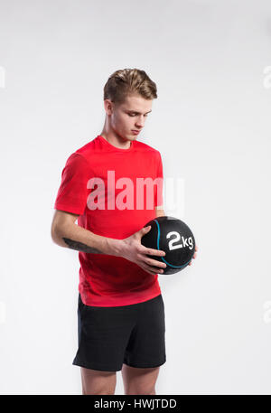Hübsche Hipster Fitness Mann im roten T-shirt mit Medicene Ball. Studio auf grauem Hintergrund gedreht. Stockfoto