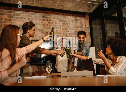 Gruppe von jungen Geschäftsleute einen Erfolg mit Bier zu feiern. Heterogene Gruppe von Menschen treffen in Startup Büro Konferenzraum Getränk Stockfoto