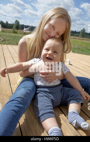 Treuen Schwester glückliches Baby Bruder auf dem Deck zu halten. Polnische Kinder Alter 8 und 7 Monate. Zawady Zentralpolen Europa Stockfoto