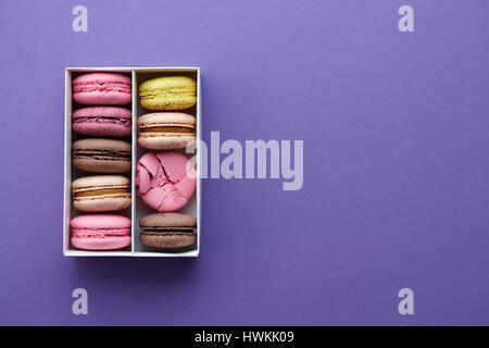 Schachtel mit bunten Macarons auf lila Hintergrund Stockfoto