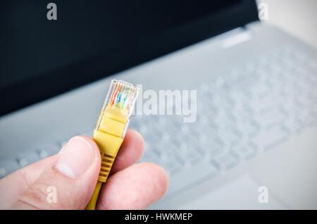 Hand mit Ethernet-Kabel. Laptop im Hintergrund Stockfoto