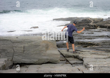 Ein Mann springt Steine in Schaumigen Wasser aus der Maine Küste Stockfoto