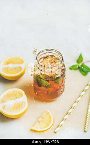 Sommer kalten Eistee mit frischer Bergamotte, Minze und Zitrone im Glas mit Spritzer auf textfreiraum Leuchttisch Hintergrund. Essen in Bewegung-Konzept Stockfoto