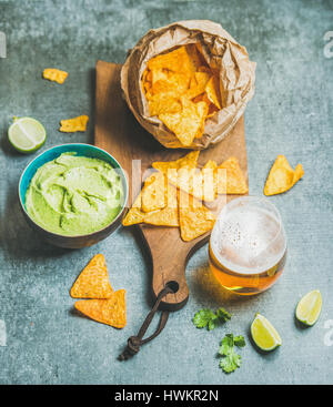 Mexikanische Mais-Chips, frische Guacamole Sauce und Glas Bier auf hölzernen Portion Brett über graue Betontisch Hintergrund, Draufsicht, selektiven Fokus Stockfoto