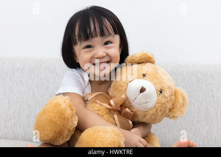 Glücklich asiatische chinesische Mädchen umarmt ein Teddy-Bär auf dem Sofa. Stockfoto