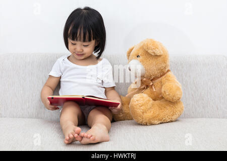 Asiatische chinesische Mädchen lesen Büchlein mit Teddy-Bär auf dem Sofa im Wohnzimmer. Stockfoto