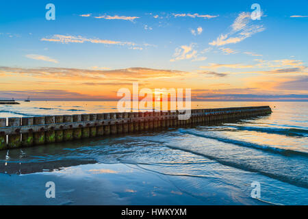 Sonnenuntergang über Meer mit hölzernen Wellenbrecher im Vordergrund Leba Strand, Ostsee, Polen Stockfoto