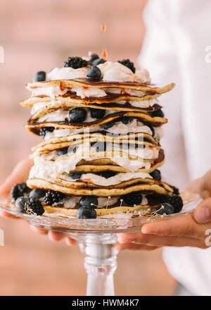 Die Frau hält in der hand Kuchen aus Pfannkuchen hautnah. Kuchen aus Pfannkuchen mit Sahne und Blaubeeren. Stockfoto