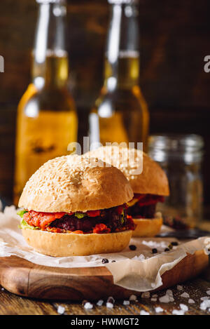 Zwei hausgemachte Rindfleisch-Burger und Flasche Bier auf Hintergrund. Stockfoto