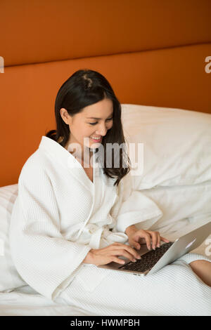 Eine asiatische Frau, die an ihrem Computer im Bett arbeitet Stockfoto