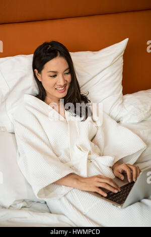 Eine asiatische Frau, die an ihrem Computer im Bett arbeitet Stockfoto