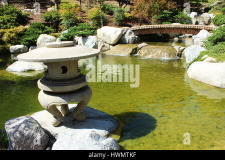 Japanische Steinlaterne, Holzbrücke über den Bach, in einem gepflegten Garten Stockfoto