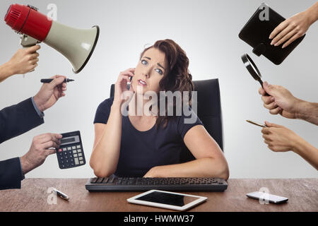 Business-Frau sitzt am Schreibtisch umgeben von vielen Händen halten von Gegenständen Stockfoto