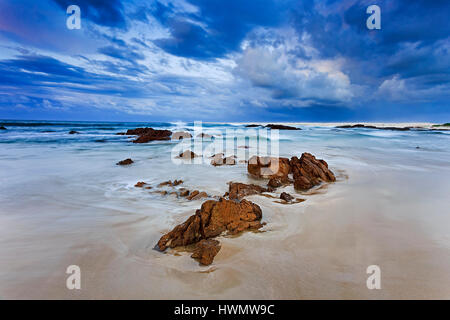 Ruhigen blau Sonnenaufgang am weißen Sandstrand mit kleinen Sandsteinfelsen bei Ebbe Wellenreiten unter dicken Wolken der australischen Küste im Pazifik gewaschene Stockfoto