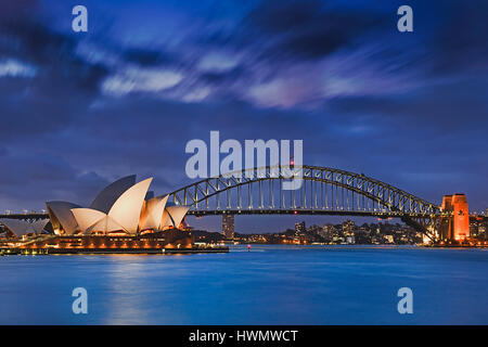 Sydney, Australien, 18. März 2017: weltweit berühmten Sydney Opera House und Harbour Bridge bei Sonnenuntergang. Verschwommenen Wolken und Lichter der Sehenswürdigkeiten spiegeln in Unschärfe Stockfoto