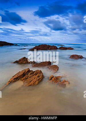 Kleine Sandstein Felsen aus personeller Surfwellen verschwommen bei Langzeitbelichtung bei Sonnenaufgang. Blaue Stunden der Pazifikküste in New South Wales, Austral Stockfoto