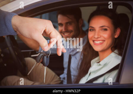 Lächelnde Frau empfangende Schlüssel von jemand gegen Porträt eines jungen Paares Road trip Stockfoto