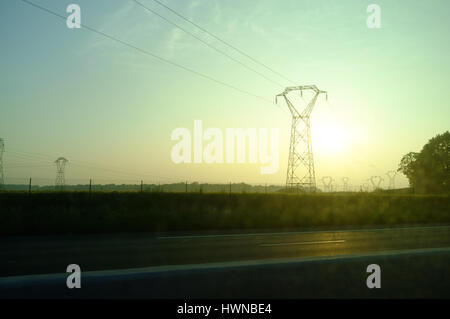 Blick auf hohe Spannung Stromleitungen während des Sonnenuntergangs auf der Autobahn, Centre-Val de Loire, Frankreich Stockfoto