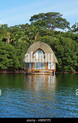 Charmante Overwater Bungalow mit Strohdach und üppiger tropischer Vegetation am Ufer des Meeres, Bocas del Toro, Panama, Karibik, Mittelamerika Stockfoto