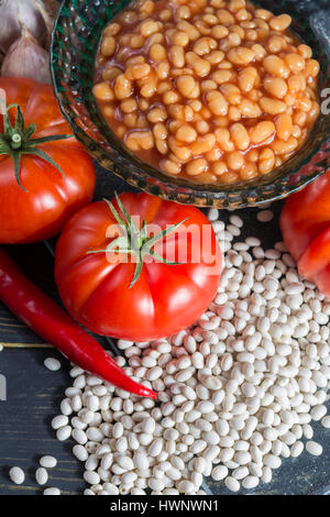 Traditionelles englisches Essen - gebackene weiße Bohnen in Tomatensauce und Zutaten bereit zu kochen - Tomaten, getrocknete weiße Bohnen und Zwiebeln Stockfoto