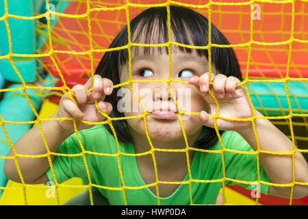 Glücklich asiatische chinesische Mädchen hinter dem Netz im indoor-Spielplatz spielen. Stockfoto