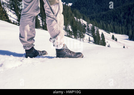 Nahaufnahme von mans Beine und Stiefel im Schnee umgeben von Bergen Stockfoto