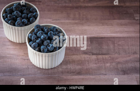 Frische leckere Blaubeeren in zwei weiße Keramik, Porzellan Schalen auf Holztisch, Oberfläche, rustikalen Stil. antioxidans organische Superfood Stockfoto