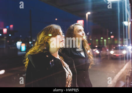 Zwei junge schöne kaukasische Frauen an der Bushaltestelle Blick durch Fenster - Freundschaft, Interaktion, Pendler-Konzept Stockfoto