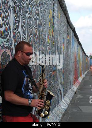 Berlin, Deutschland - 2013. Juli 30: Einseitiger Saxophonist lehnte sich gegen Reste der Berliner Mauer, die East Side Gallery genannt wird Stockfoto