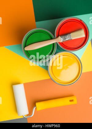 drei Dosen gelb, grün und rot und Lack Pinsel und Rollen auf bunten geometrischen Hintergrund Stockfoto