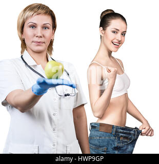 Arzt hält grünen Apfel. Junge Frau zeigt Gewicht-Verlust-Ergebnis. Gesunde Ernährung-Konzept. Stockfoto