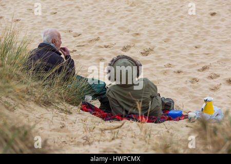 Sandbänke, Poole - paar mit einem Picknick am Strand von Sandbänken Poole, Dorset, Großbritannien im März Warm eingepackt Stockfoto