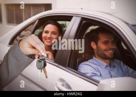 Person, die Schlüsselübergabe an jemand anderen gegen junges Paar Lächeln beim Sitzen im Auto Stockfoto