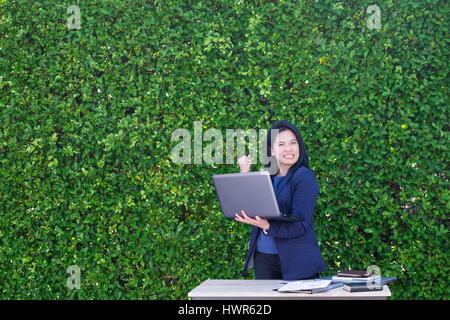 Geschäftsfrau Arm bis zum Business Plan Erfolg außerhalb Büro im grünen Blatt Wand zu feiern. Stockfoto
