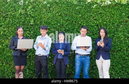 Unternehmerin und Unternehmer arbeiten außerhalb Büro grünes Blatt Wand, mobilen Bürokonzept, Laptop-Computer-Handy und Tablet-Gerät mit cop Stockfoto