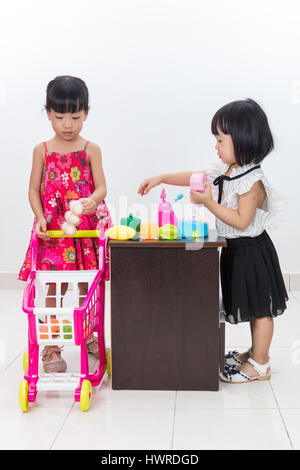 Asiatische chinesische kleine Schwestern so zu tun als Kassierer und Kunden mit Trolley Spielzeug in isolierten weißen Hintergrund. Stockfoto